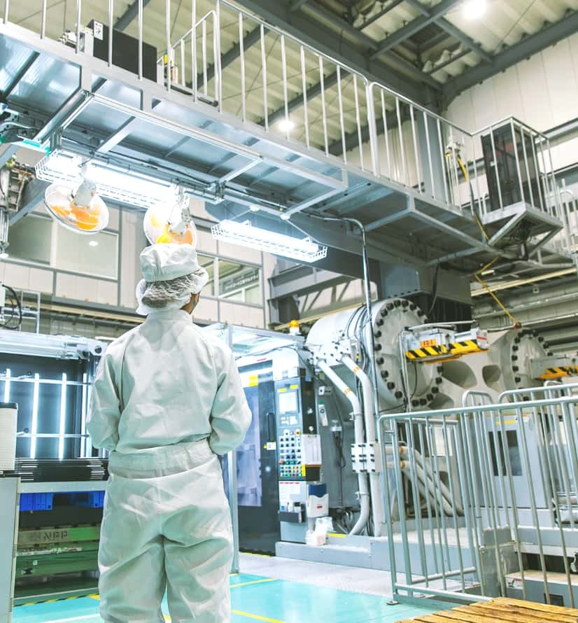白い作業着と帽子を身につけ、工場の機械に囲まれて佇んでいる社員の写真