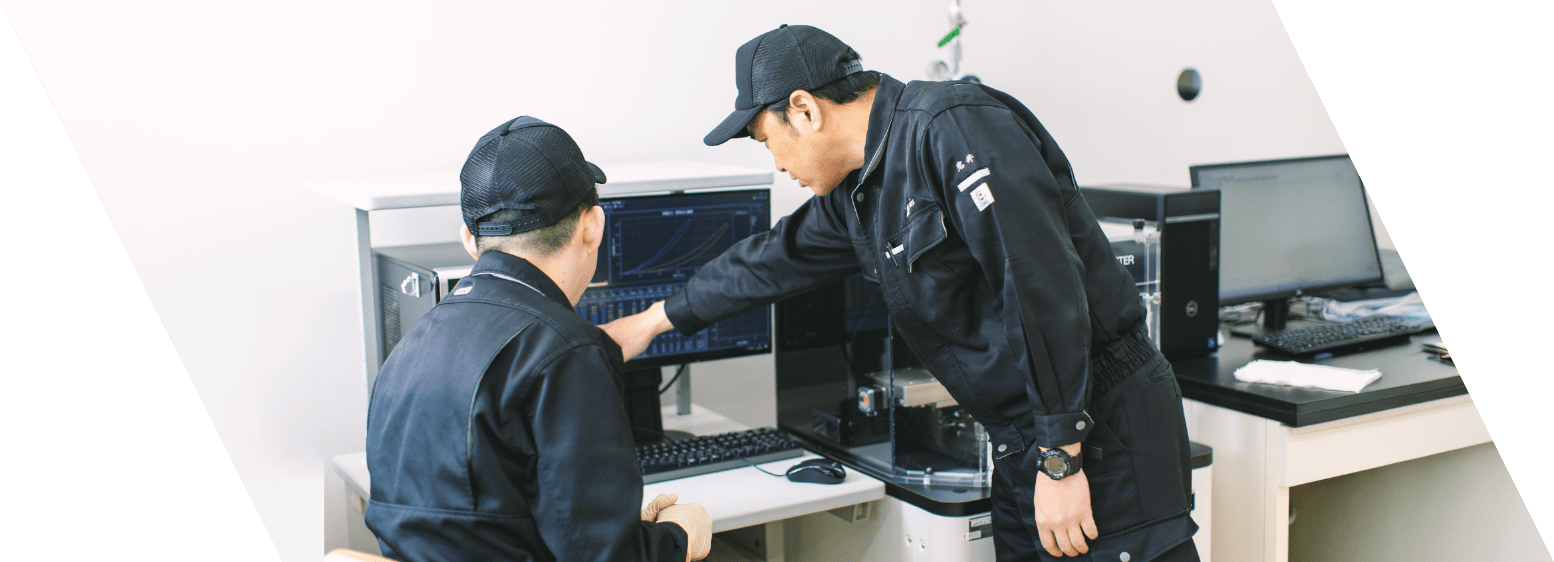 黒い作業着を着たスタッフ2名がPC画面を見ながら何かを話している写真